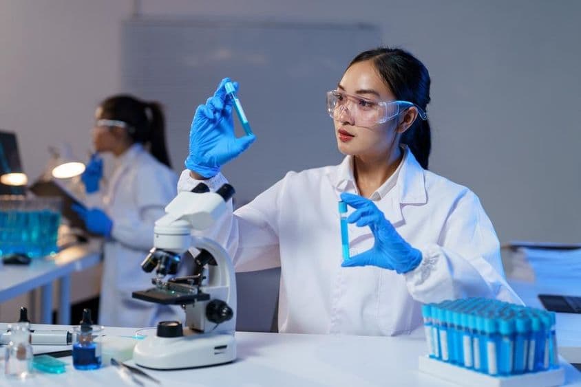 Scientifique asiatique en blouse de laboratoire et gants comparant deux tubes à essai.
