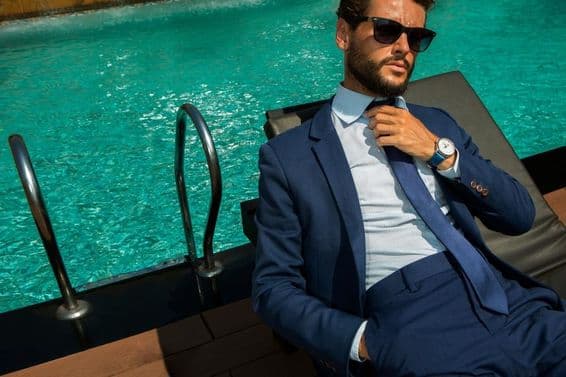 Homme d'affaires prospère en costume bleu classique près d'une piscine de luxe.