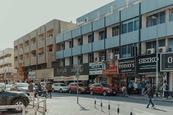 Rue animée dans Bur Dubai avec des bijouteries, des piétons et des voitures par une journée ensoleillée.