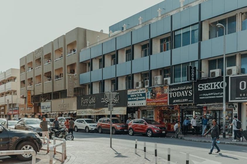 Rue animée dans Bur Dubai avec des bijouteries, des piétons et des voitures par une journée ensoleillée.