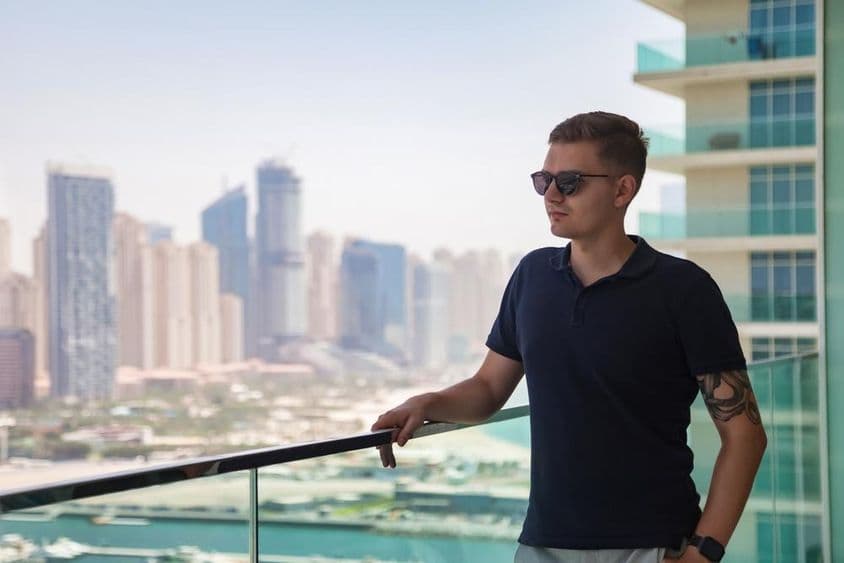 Un jeune homme en lunettes de soleil sur un balcon de gratte-ciel surplombant Dubaï.