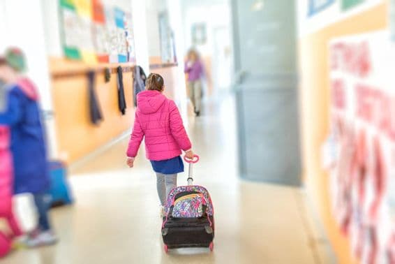 Une jeune fille tire un cartable scolaire à roulettes.