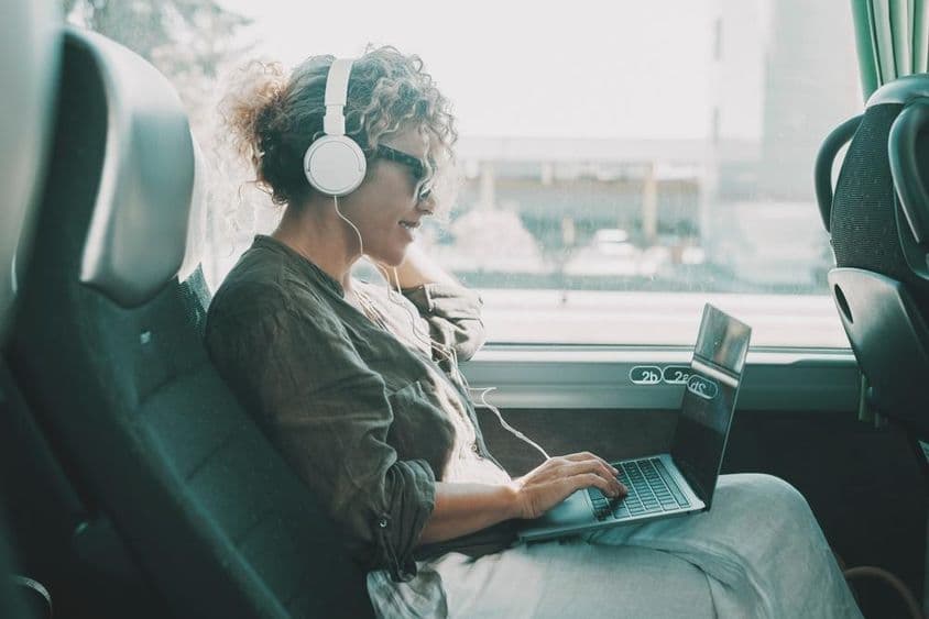 Jeune femme travaillant sur un ordinateur portable avec des écouteurs sur un siège de bus.