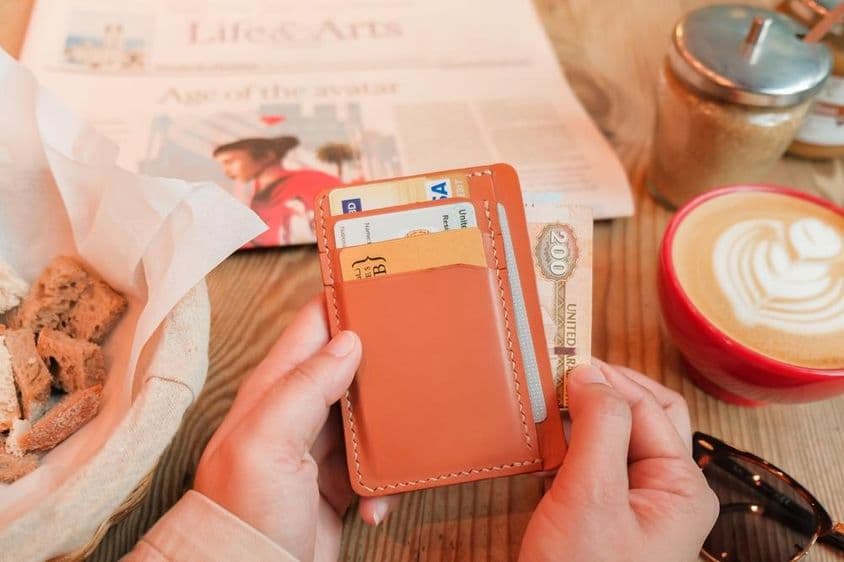 Une main tirant 200 dirhams des Émirats arabes unis d'un porte-cartes en cuir marron.