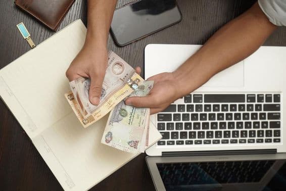 Un homme comptant une liasse de billets de banque en dirhams des Émirats Arabes Unis.