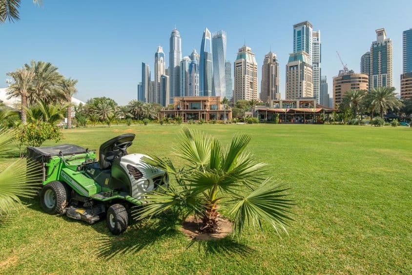 Tracteur tondeuse sur un champ vert devant les gratte-ciels de Dubai Marina.