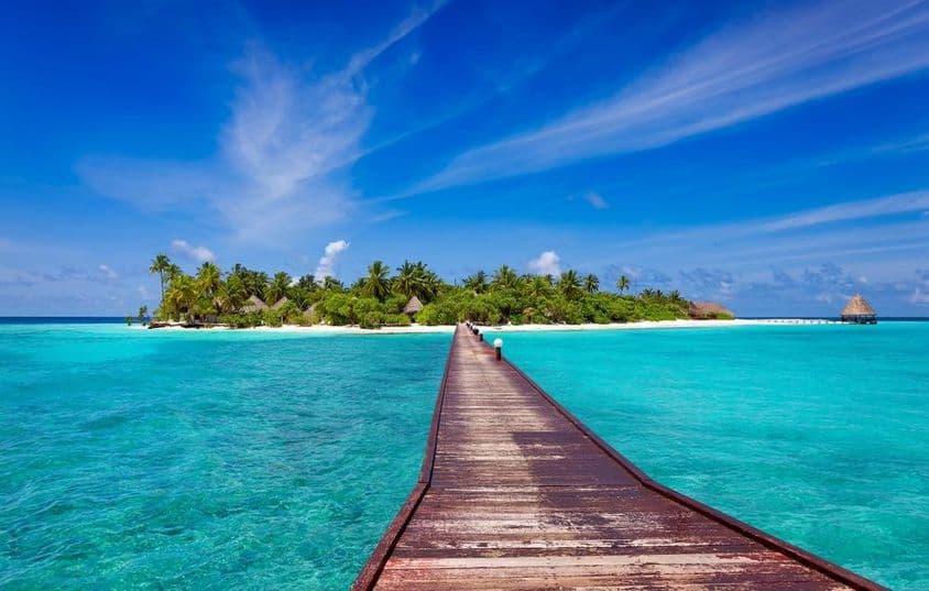 Jetée sur un océan bleu menant à la plage de sable d'une île tropicale, Maldives.