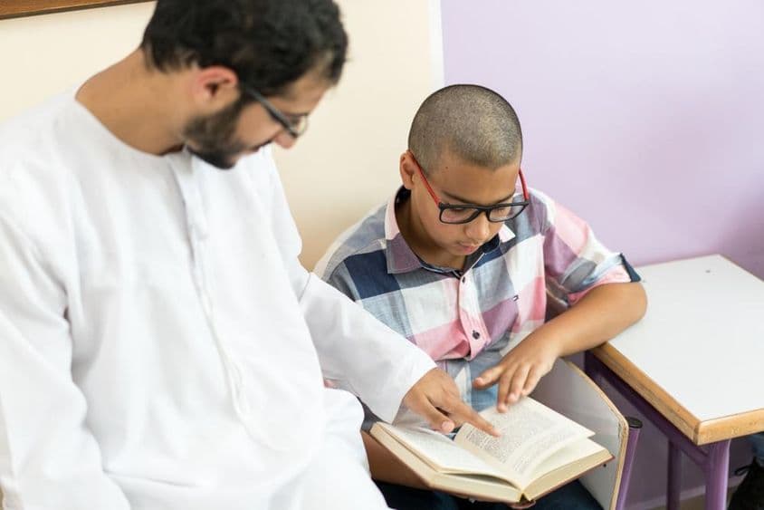 Jeune enseignant arabe étudiant avec un écolier.