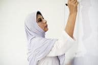 Un enseignant musulman écrivant sur un tableau blanc.