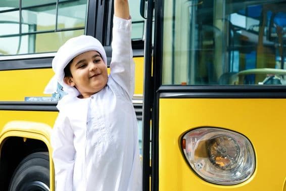 Élève d'école primaire arabe près d'un bus scolaire jaune.