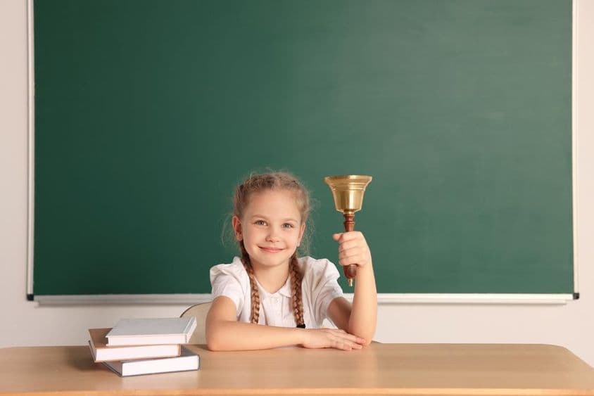Élève assis à un bureau avec la cloche scolaire dans une salle de classe.