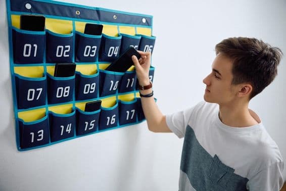 Un étudiant laisse son smartphone dans un organisateur de téléphone mural.