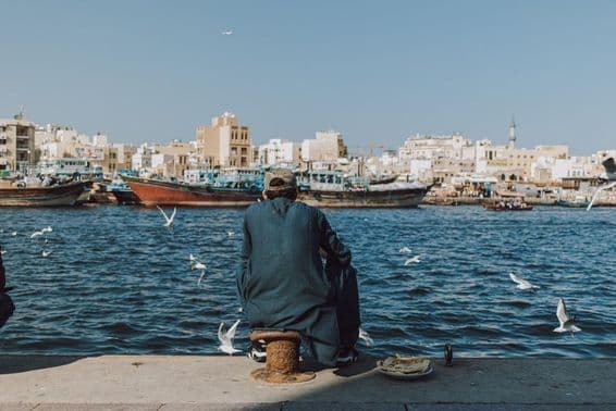 Homme profitant de la vue sur le front de mer avec des bateaux et des mouettes à Dubai Creek.