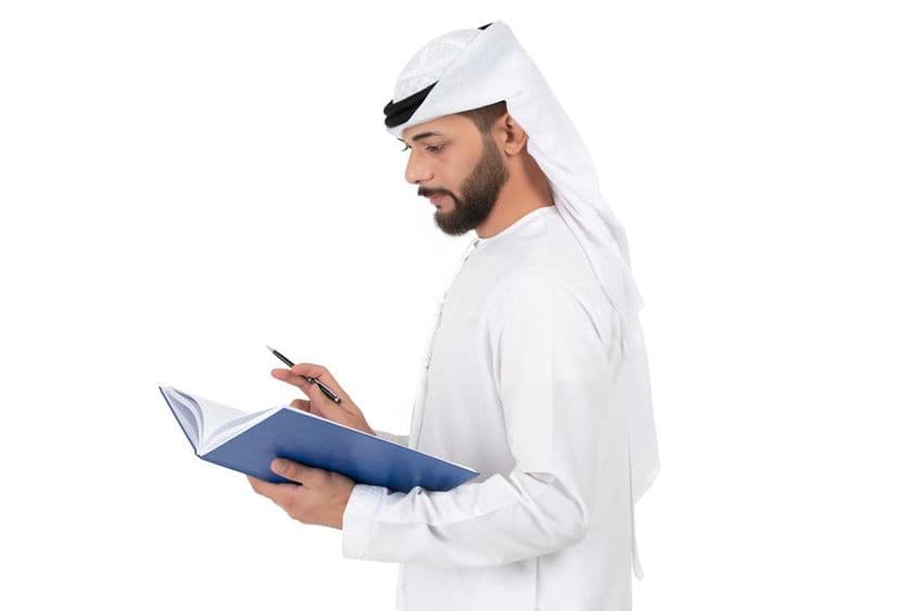 Jeune enseignant arabe debout et écrivant dans le livre.