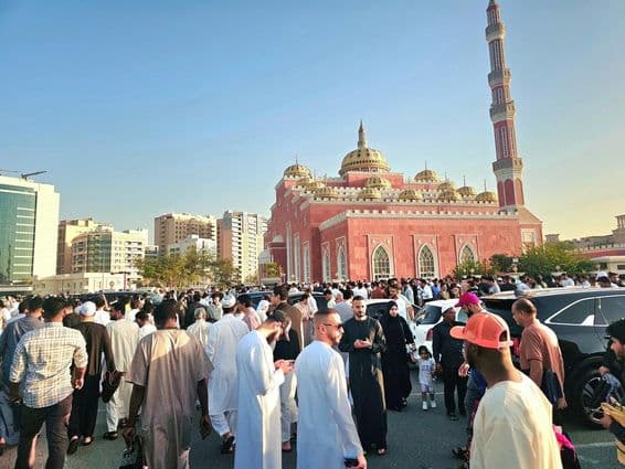 Une grande foule rassemblée devant une grande mosquée avec des dômes et de hauts minarets.