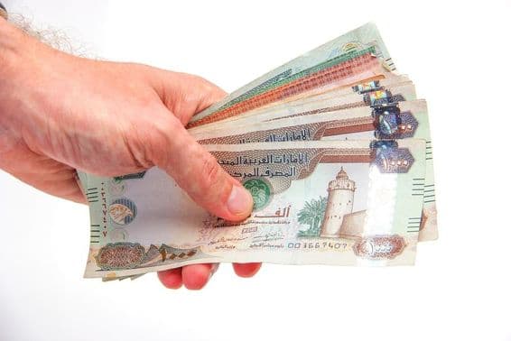Un homme tenant des billets de dirhams des Émirats arabes unis.