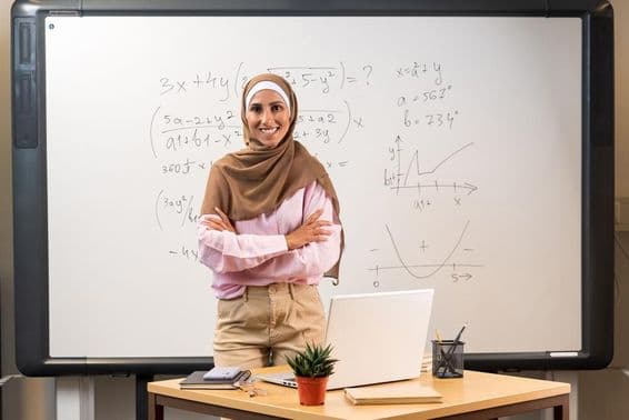 Enseignante arabe en hijab se tenant dans une classe.