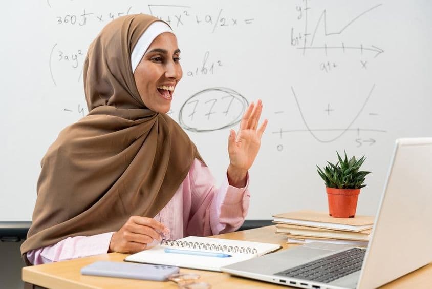 Enseignante en hijab saluant des étudiants lors d'une classe en ligne.