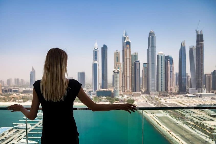 Une femme en noir avec un regard pensif sur un balcon surplombant les gratte-ciel de Dubaï, Émirats Arabes Unis.