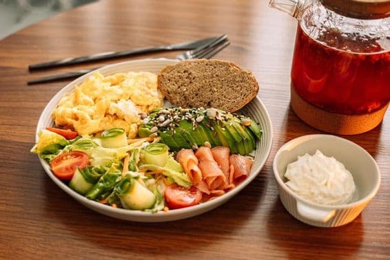 Petit-déjeuner santé avec des œufs, avocat, légumes verts, salade, et thé à la framboise.