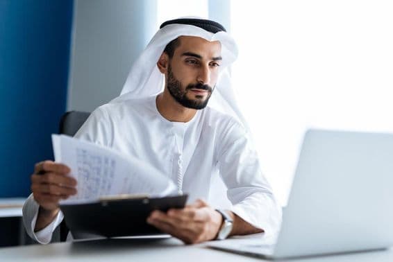 Homme travaillant avec un ordinateur portable dans un bureau à Dubaï, vêtu de la tenue blanche traditionnelle émiratie.