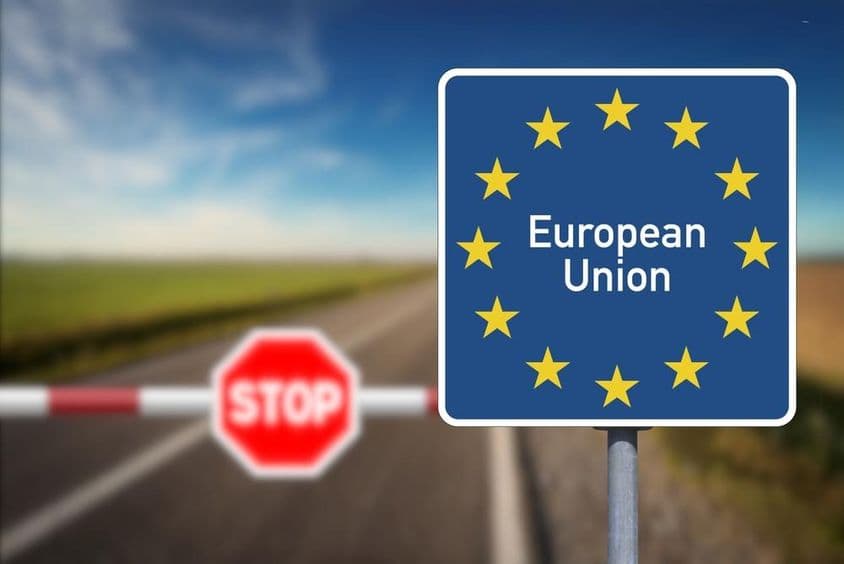 Emblème de l'Union européenne et un passage frontalier avec barrière et panneau stop.