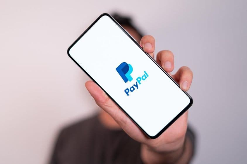 Un homme tenant un téléphone avec le logo PayPal visible à l'écran.