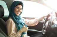 Femme arabe heureuse en hijab conduisant sa voiture avec un pouce levé.