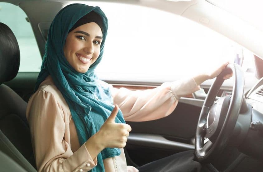 Femme arabe heureuse en hijab conduisant sa voiture avec un pouce levé.