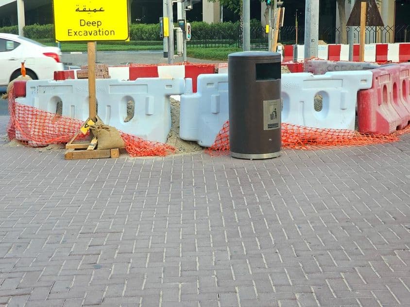 La réparation routière est entourée de barrières en plastique et d'un filet de sécurité orange.