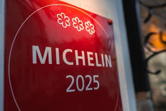Une plaque Michelin rouge trois étoiles 2025 sur un mur clair.