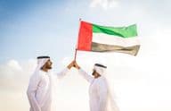 Des hommes arabes vêtus de kanduras marchant dans le désert en tenant un drapeau.