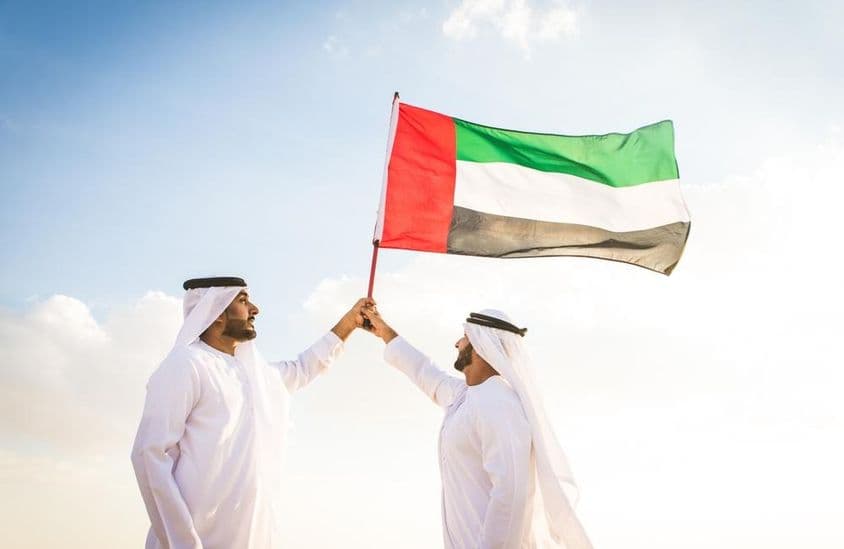 Des hommes arabes vêtus de kanduras marchant dans le désert en tenant un drapeau.