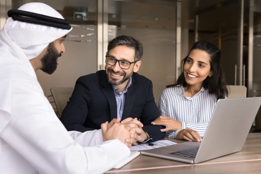 Un couple latin heureux rencontrant un agent immobilier arabe.