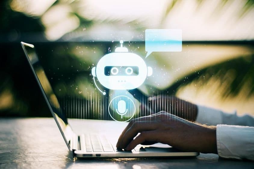 Une personne tapant sur un ordinateur portable avec un arrière-plan flou en extérieur mettant en scène une icône de chatbot.