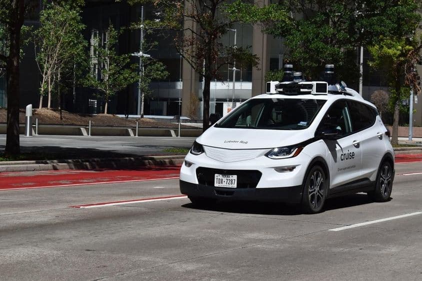 Une voiture autonome blanche sous supervision circulant dans le quartier financier du centre-ville.