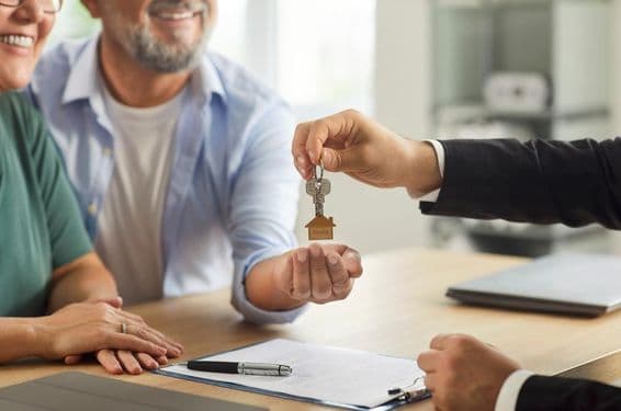 Agent immobilier remettant des clés à un couple âgé souriant.