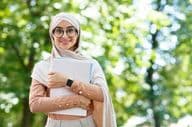 Retour à l'école, une femme arabe en hijab et lunettes tenant des livres dans un parc.