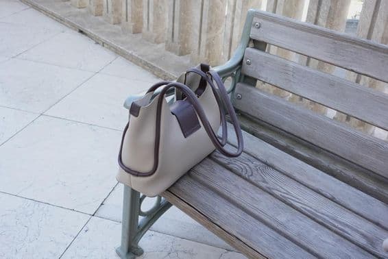 Sac posé sur un banc en bois dans un cadre urbain.