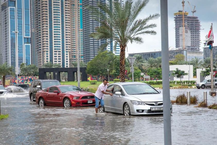 Des personnes poussant des voitures hors de l'eau dans des rues inondées à Dubaï.