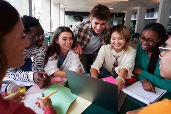 Un groupe joyeux d'étudiants universitaires assis à une table regardent un cahier.