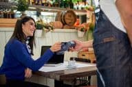Femme aux cheveux bruns assise dans un café, payant avec une carte de crédit.