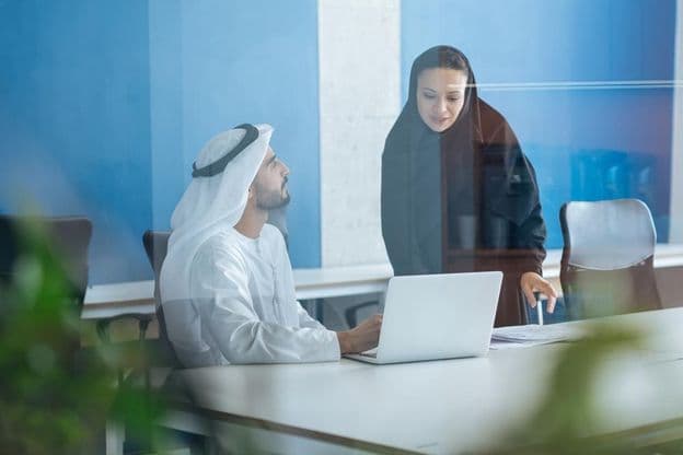 Homme et femme en tenue traditionnelle travaillant dans un bureau d'affaires à Dubaï.