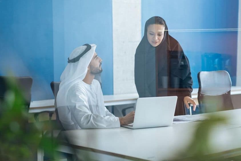 Homme et femme en tenue traditionnelle travaillant dans un bureau d'affaires à Dubaï.