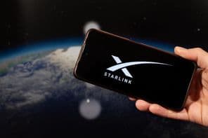 Main d'un homme tenant un smartphone avec un logo Starlink dans la main droite.