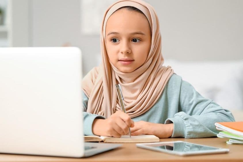 Petite fille musulmane faisant ses devoirs à la maison en portant un hijab.