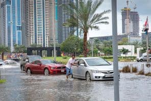 Personnes poussant des voitures dans l'eau sur des rues inondées à Dubaï.