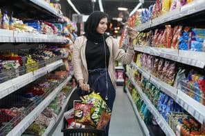 Une jeune femme arabe regarde des snacks dans un supermarché.
