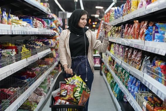 Une jeune femme arabe regarde des snacks dans un supermarché.