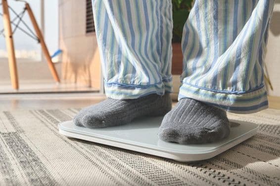 Homme en pyjama rayé debout sur une balance numérique blanche